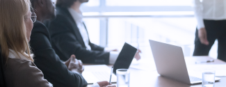 Photo of business people seated around a conference table with laptops opened.